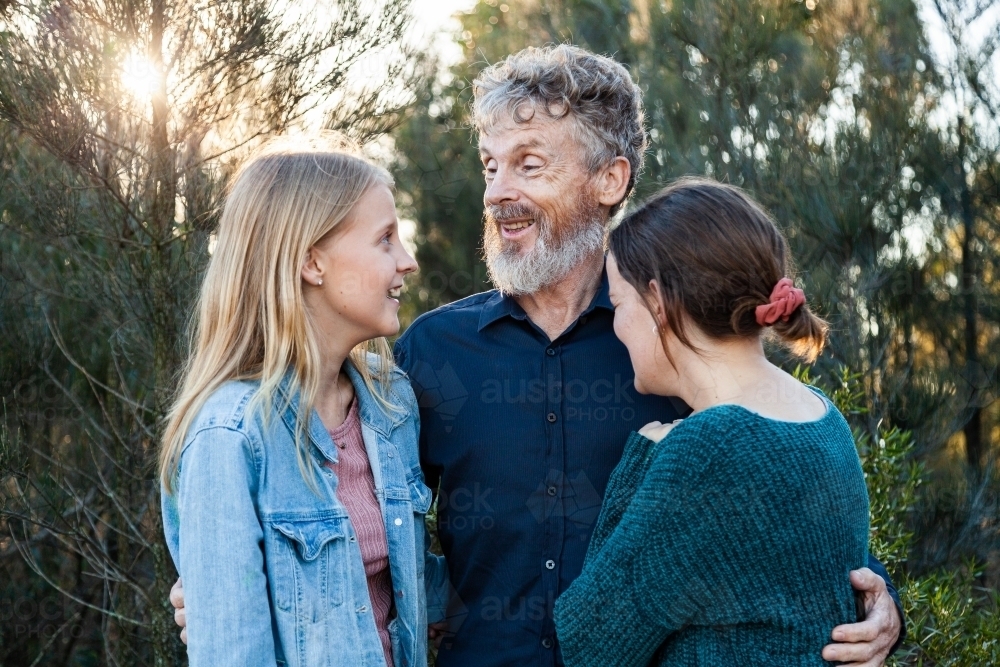 Happy dad with his two teenage daughters hug together outside - Australian Stock Image