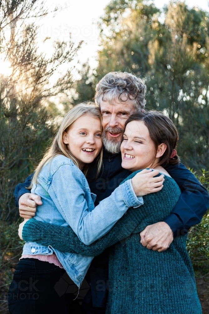 Happy dad with his two teenage daughters hug together outside - Australian Stock Image