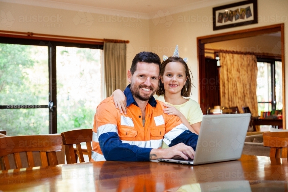 Happy dad working on laptop from home with young daughter - Australian Stock Image