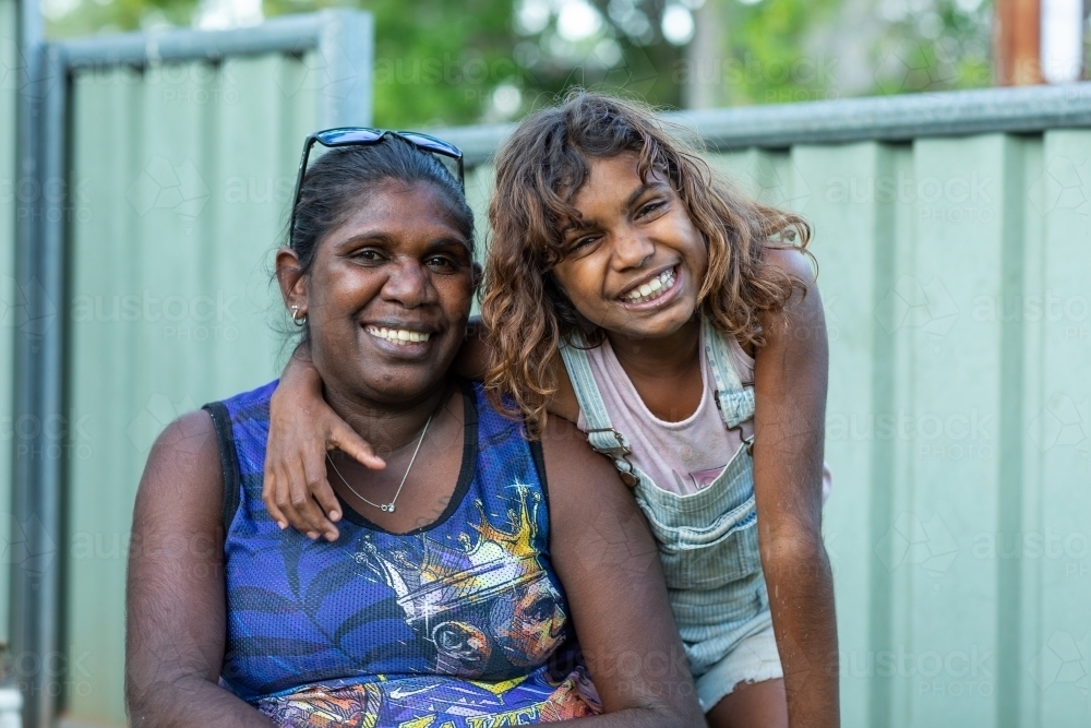 Happy daughter draping arm around mother's neck outside - Australian Stock Image