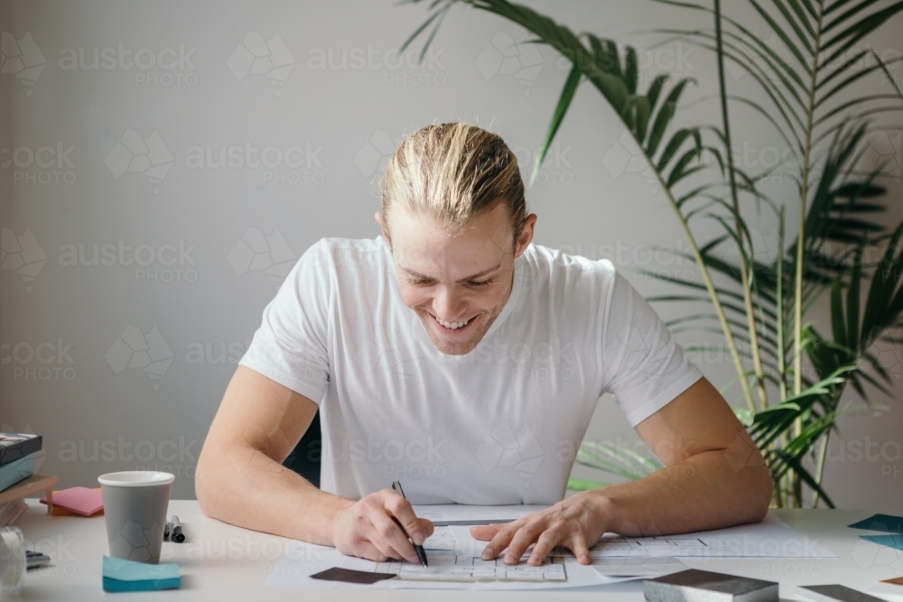 Happy designer working at a desk with indoor plant behind - Australian Stock Image