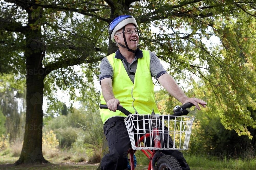 Happy disabled man wearing helmet and high visibility vest riding bike - Australian Stock Image