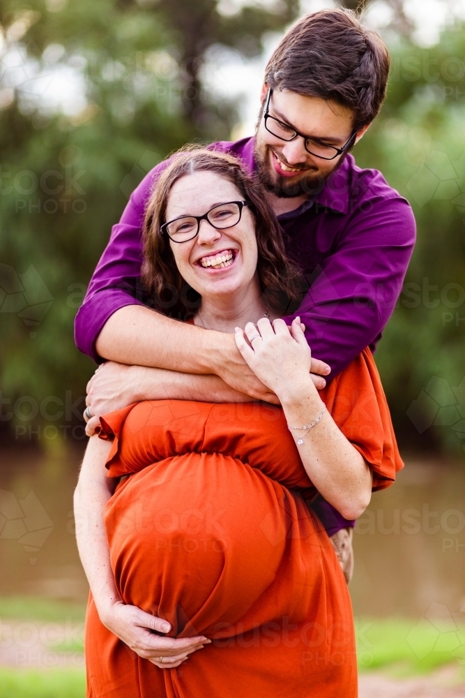 Happy expectant couple husband holding wife with her arm on pregnant belly - Australian Stock Image