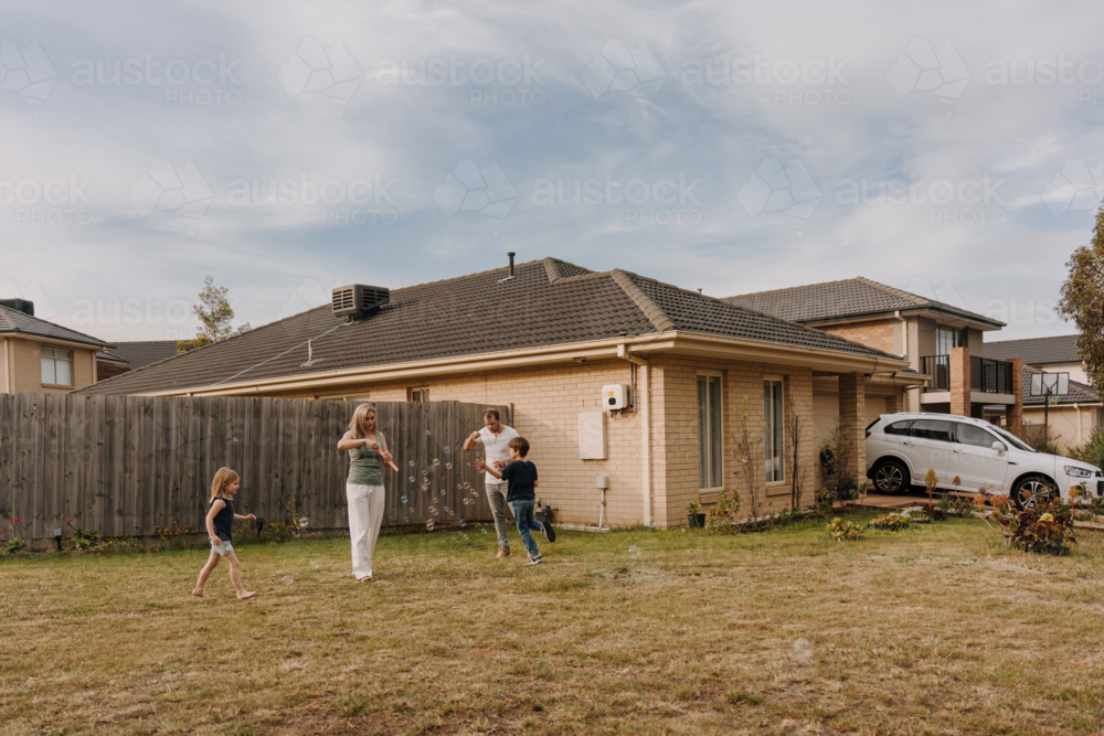 Happy family blowing and playing with bubbles in their yard. - Australian Stock Image