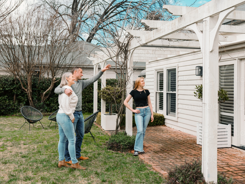 Happy family gathered in the patio of their new home with adult man pointing towards patio rafter - Australian Stock Image