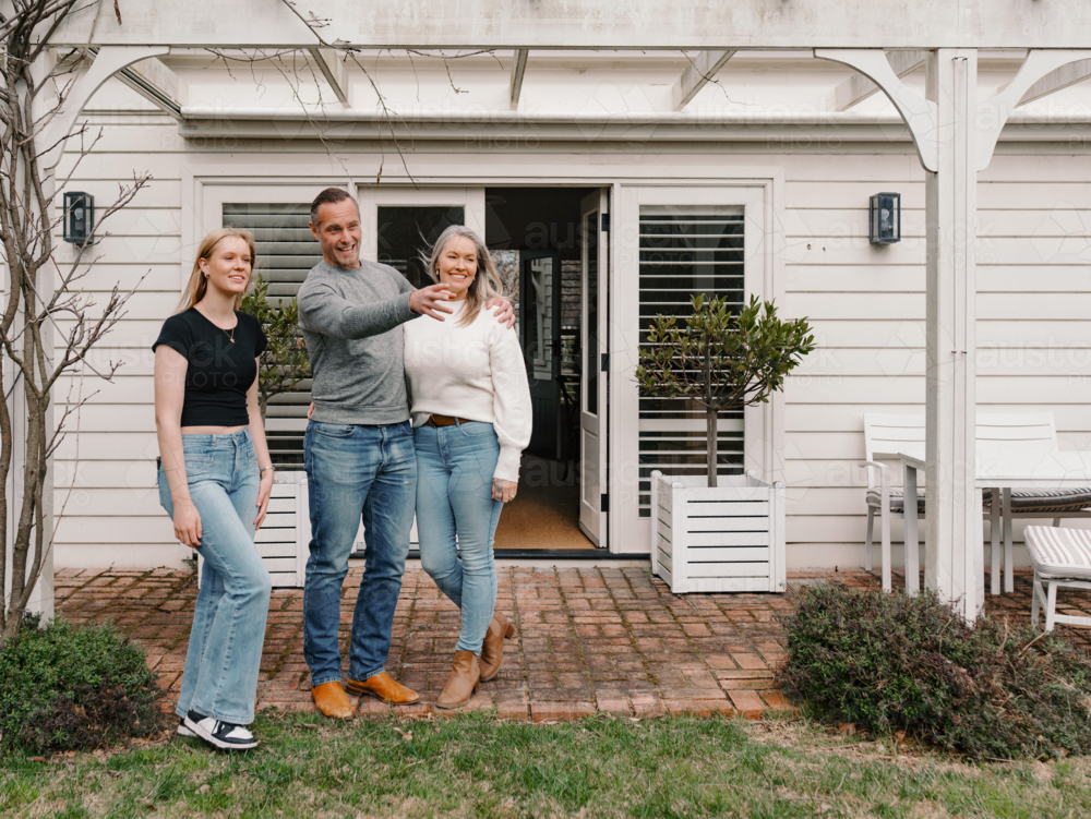 Happy family gathered in the patio of their new home with adult man pointing towards the garden - Australian Stock Image