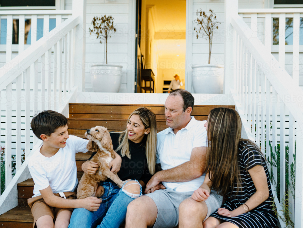 Happy family sitting outside on the steps of their house. - Australian Stock Image