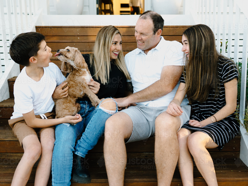 Happy family sitting outside on the steps of their house. - Australian Stock Image