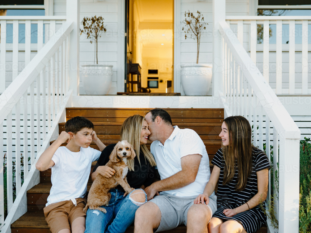 Happy family sitting outside on the steps of their house. - Australian Stock Image