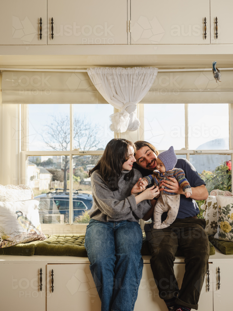 Happy family sitting together near windows inside brightly lit home - Australian Stock Image