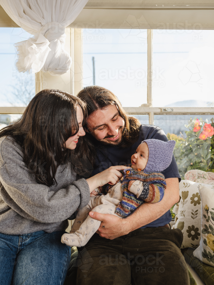 Happy family sitting together near windows inside brightly lit home - Australian Stock Image