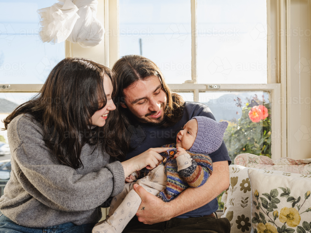Happy family sitting together near windows inside brightly lit home - Australian Stock Image