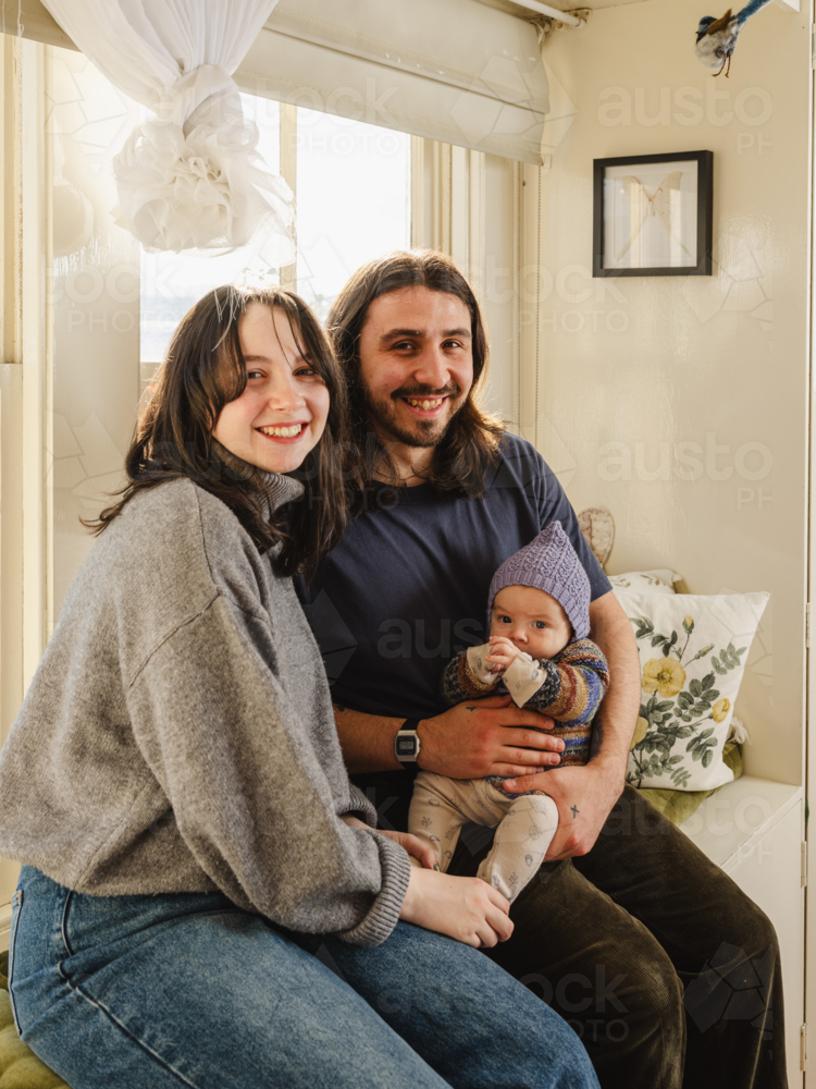 Happy family sitting together near windows inside brightly lit home - Australian Stock Image