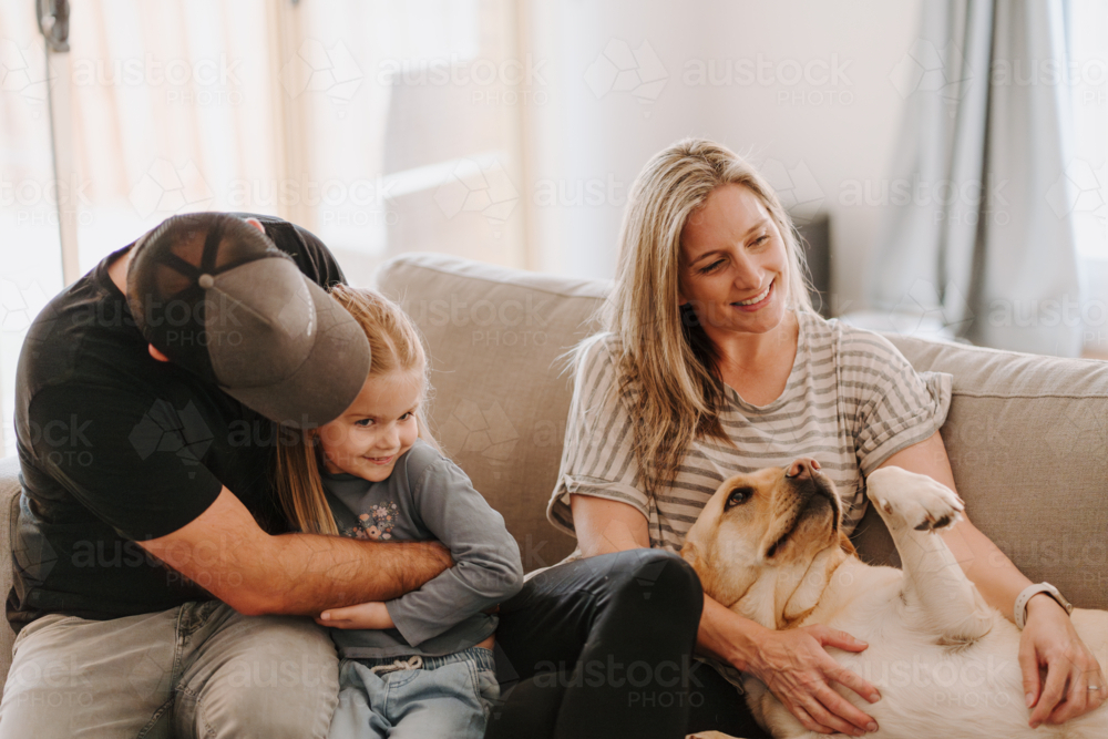 Happy family snuggles on the couch with their pet dog - Australian Stock Image