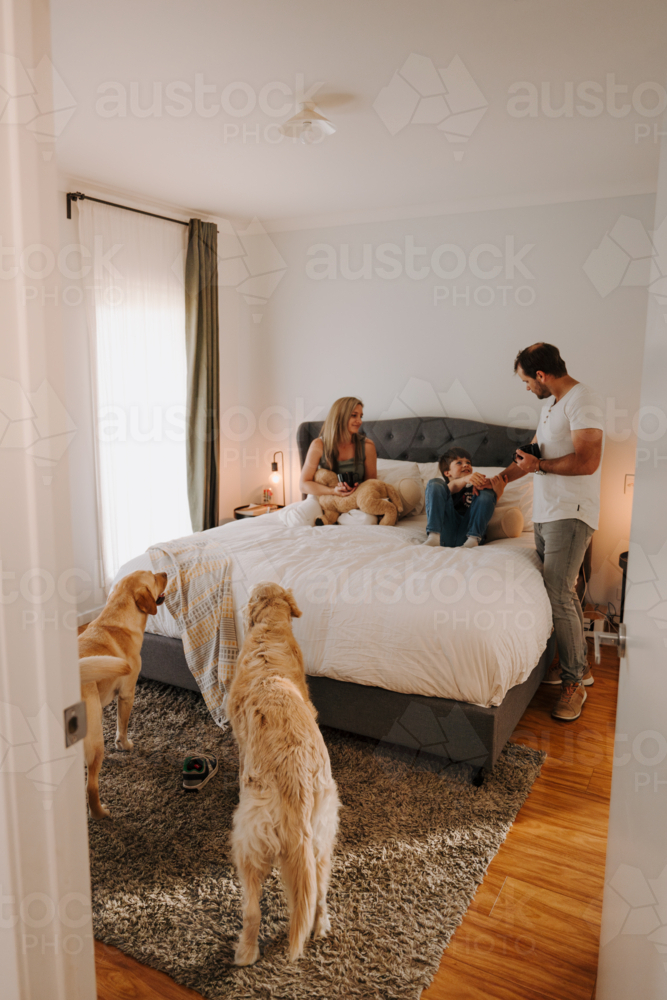 Happy family snuggling in a cosy bed. - Australian Stock Image
