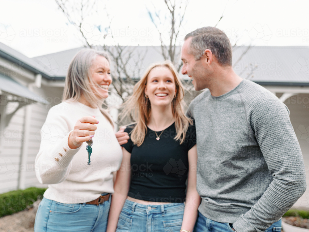 Happy family standing in front yard with mum holding out the key of their new home - Australian Stock Image