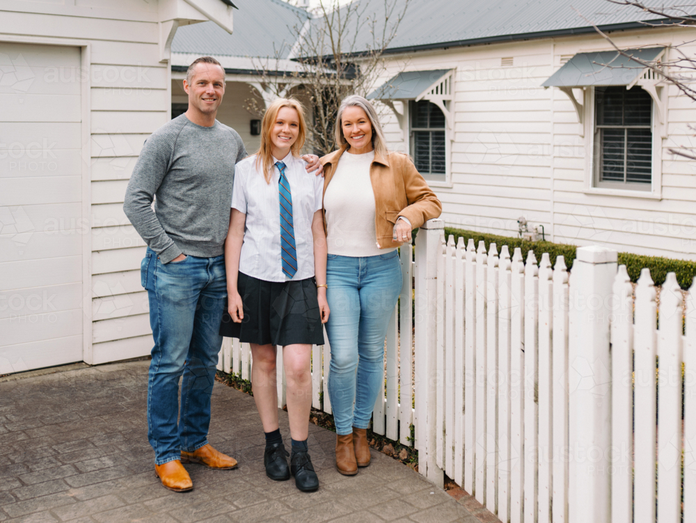 Happy family standing outside the white picket fence of their new home - Australian Stock Image
