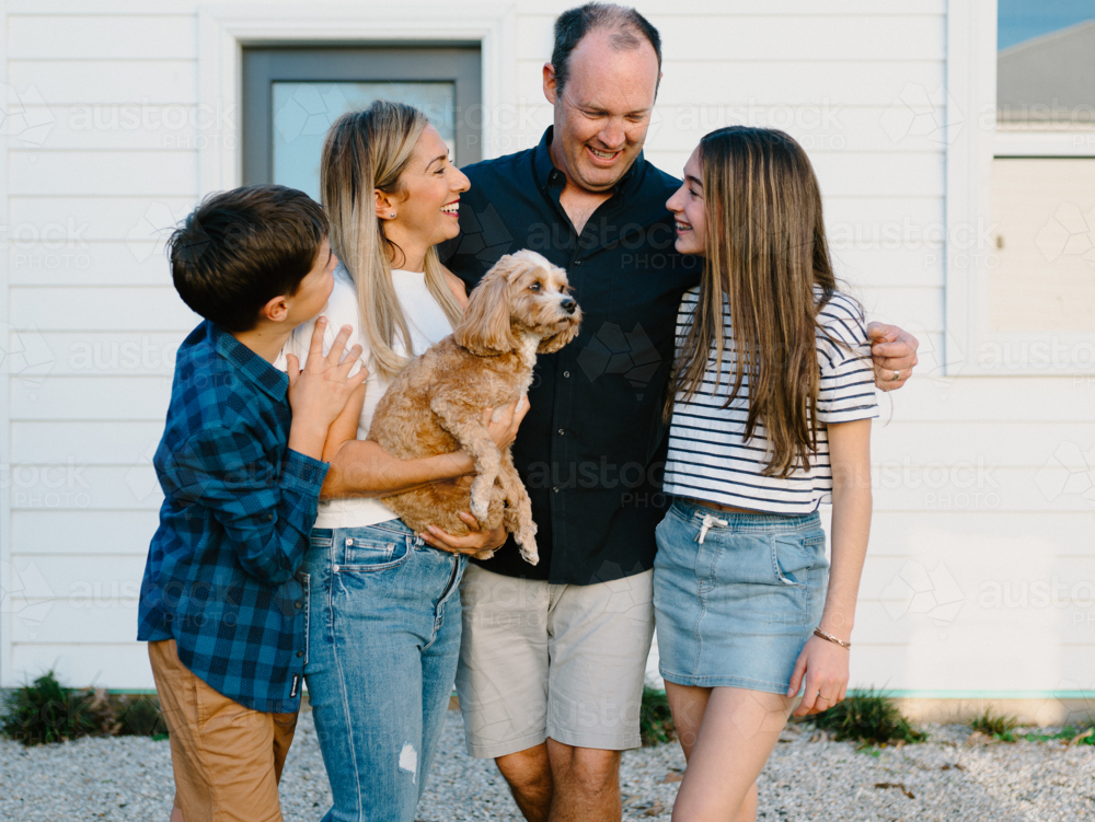 Happy family standing outside their home with their dog. - Australian Stock Image