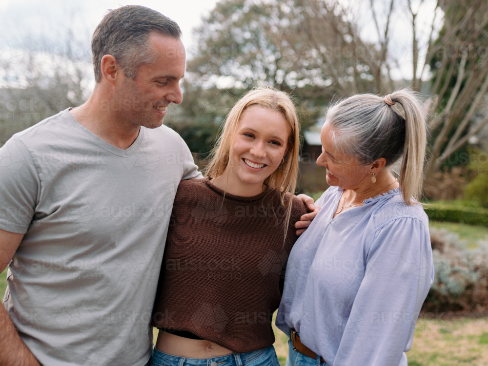 Happy family stands closely hugging each other in the garden of their new home - Australian Stock Image