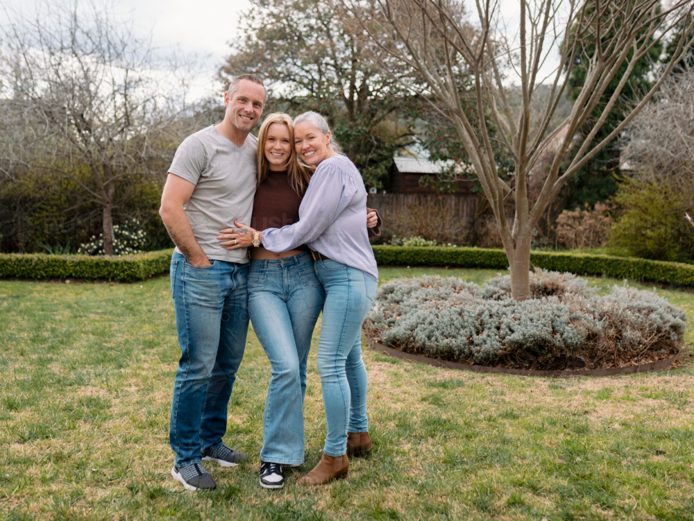 Happy family stands closely hugging each other in the garden of their new home - Australian Stock Image