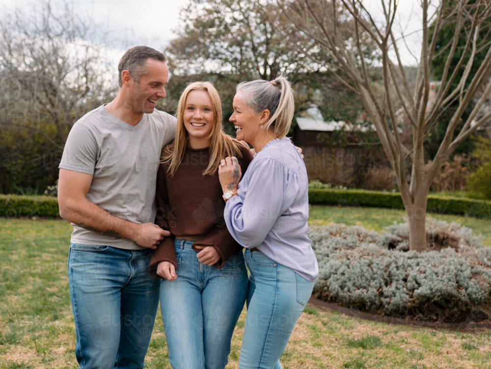 Happy family stands closely hugging each other in the garden of their new home - Australian Stock Image