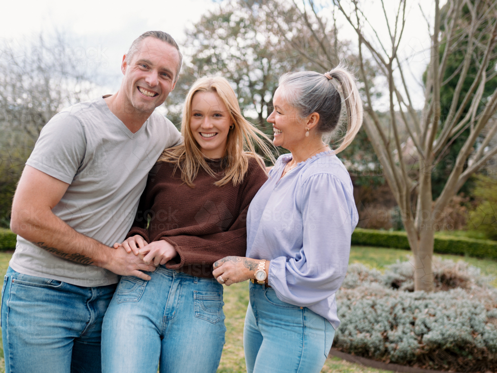 Happy family stands closely hugging each other in the garden of their new home - Australian Stock Image