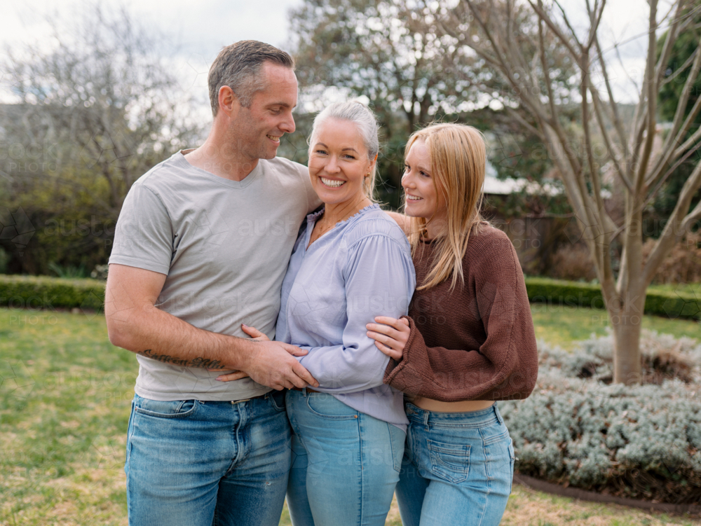 Happy family stands closely hugging each other in the garden of their new home - Australian Stock Image