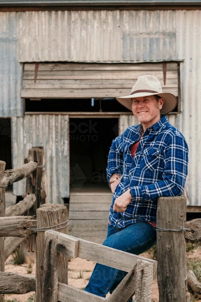 Happy farmer leans against sheep yards. - Australian Stock Image