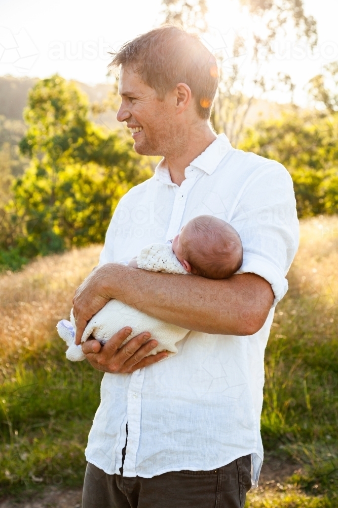 Happy father holding newborn baby girl in sunlight outside - Australian Stock Image