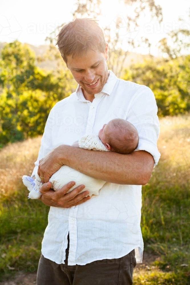 Happy father holding newborn baby girl in sunlight outside - Australian Stock Image