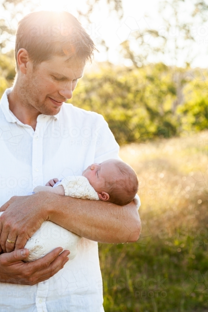 Happy father holding newborn baby girl in sunlight outside - Australian Stock Image