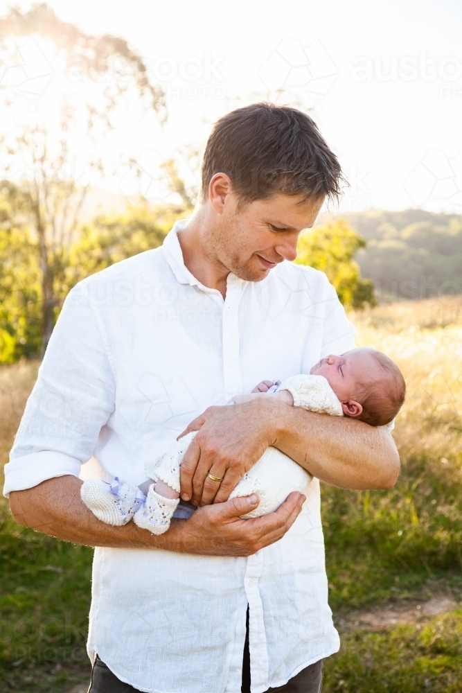 Happy father holding newborn baby girl in sunlight outside - Australian Stock Image