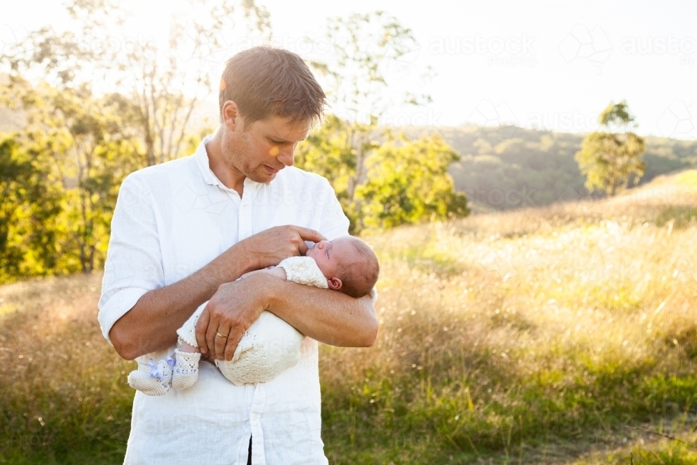 Happy father holding newborn baby girl in sunlight outside - Australian Stock Image