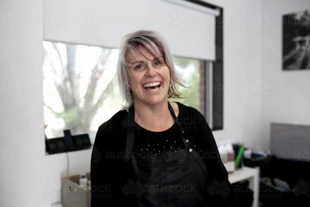 Happy female hairdresser laughing with salon in background - Australian Stock Image
