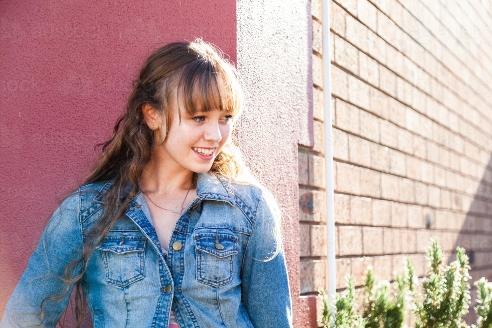 Happy female teenager wearing denim jacket in urban setting - Australian Stock Image