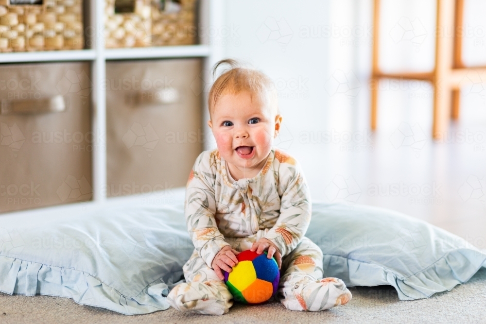 Happy five month old baby learning to sit playing with ball - Australian Stock Image