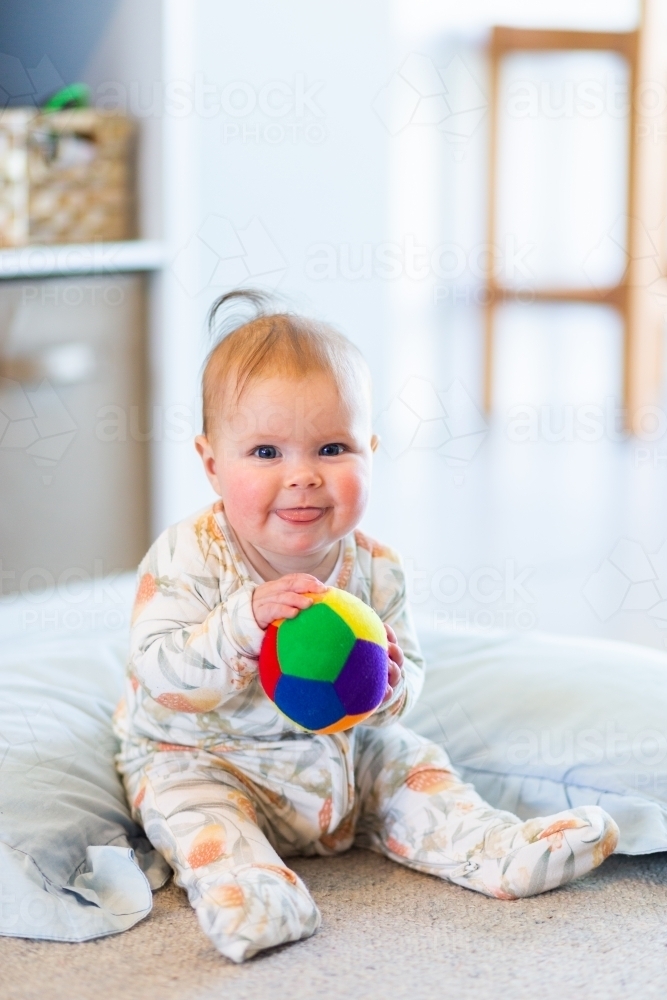 Happy five month old baby learning to sit up playing with colourful ball - Australian Stock Image