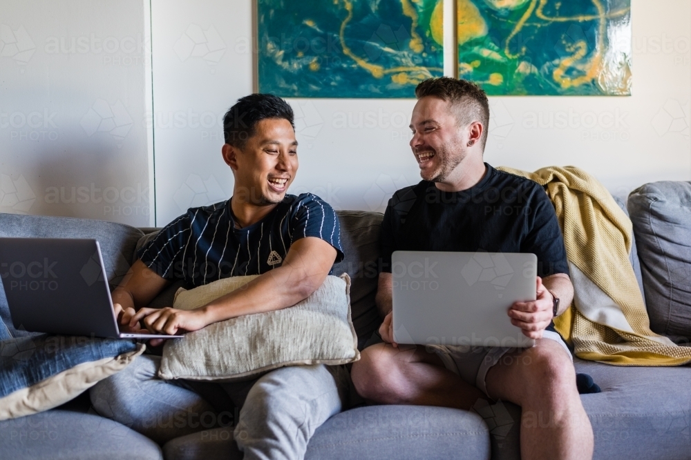 Happy gay couple at home, with laptops - Australian Stock Image