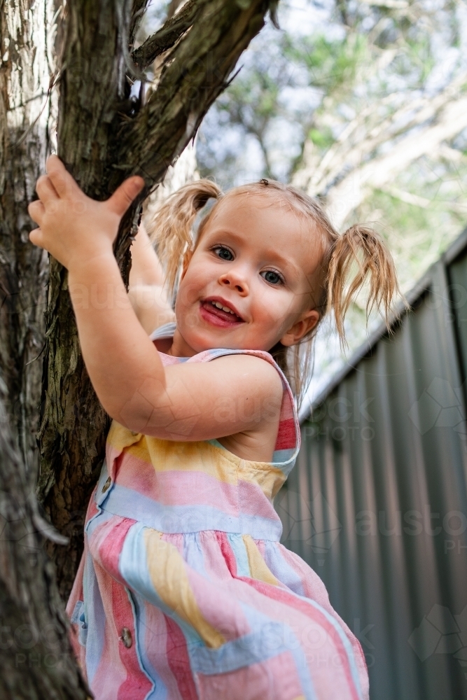 Happy girl in pastel dress climbing tree - Australian Stock Image