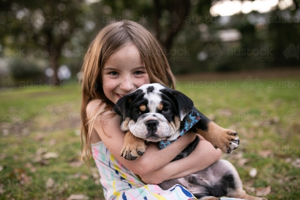 Happy girl outside holding pet bulldog puppy - Australian Stock Image