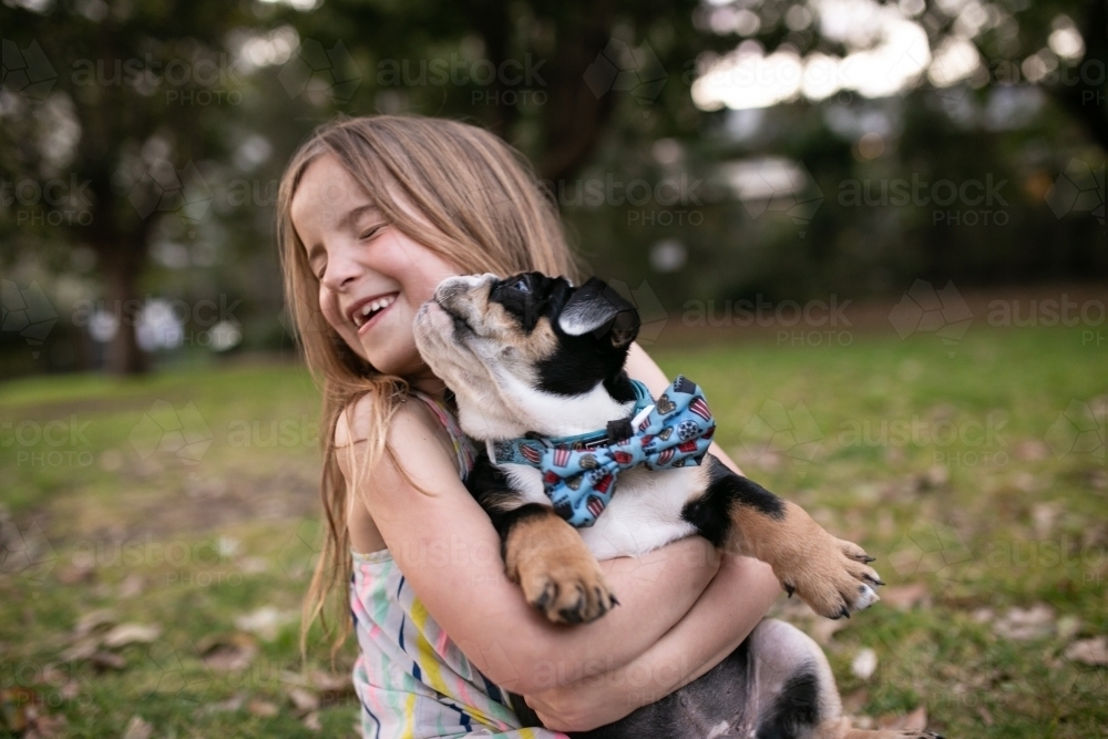 Happy girl outside holding pet bulldog puppy laughing together - Australian Stock Image