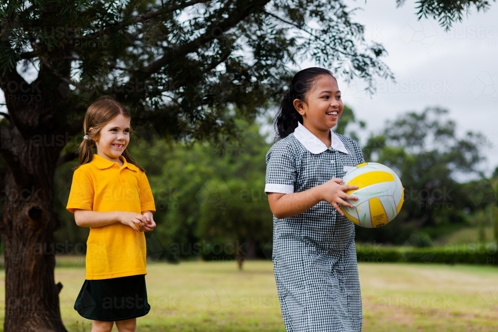 Happy girls laughing outside while playing ball game at school - Australian Stock Image