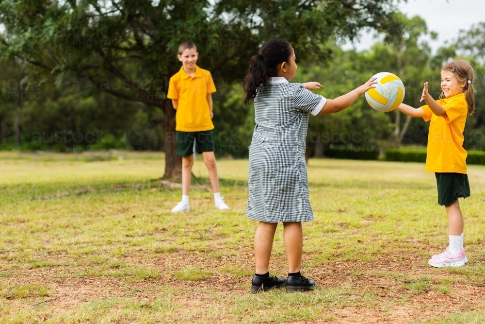Happy healthy school kids throwing a ball to one another outside - Australian Stock Image