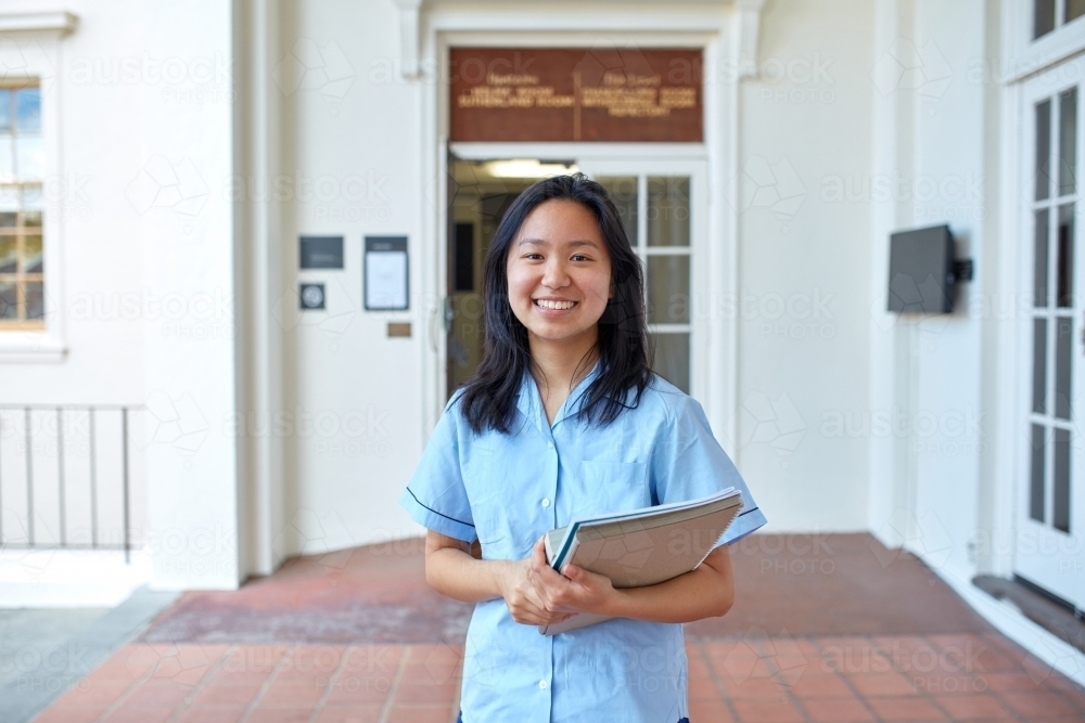 Happy High School student holding text books on-campus - Australian Stock Image