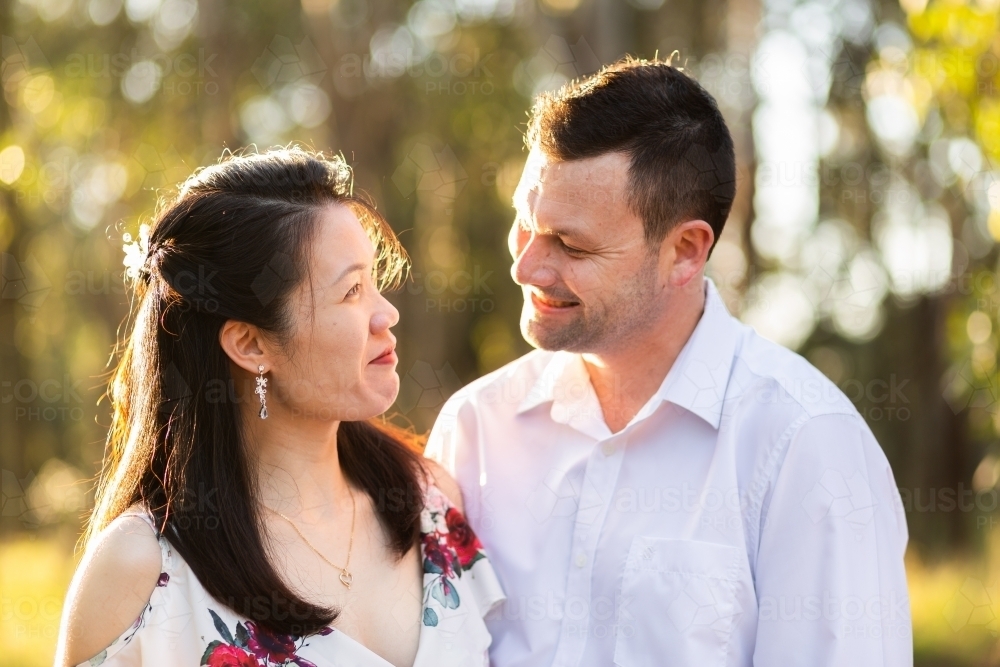 Happy interracial couple looking at one another smiling in sunlight - Australian Stock Image