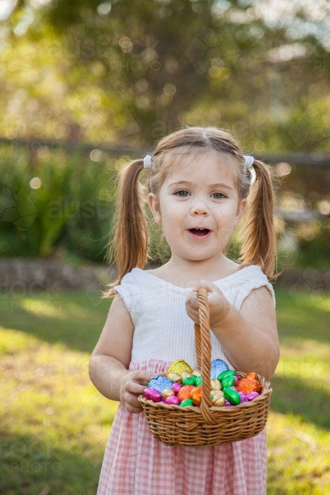 Happy kid holding basket of bright coloured Easter eggs found on an Easter egg hunt - Australian Stock Image
