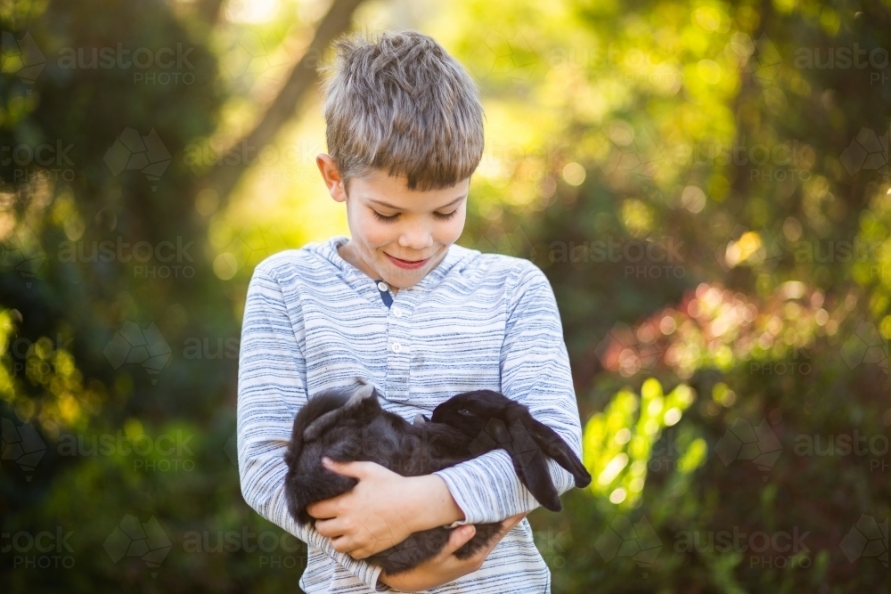 Happy kid holding his pet black bunny rabbit - Australian Stock Image