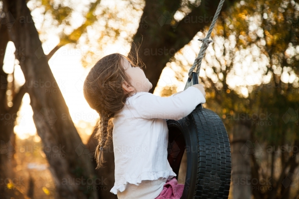 Happy kid playing in backyard on tyre swing - Australian Stock Image