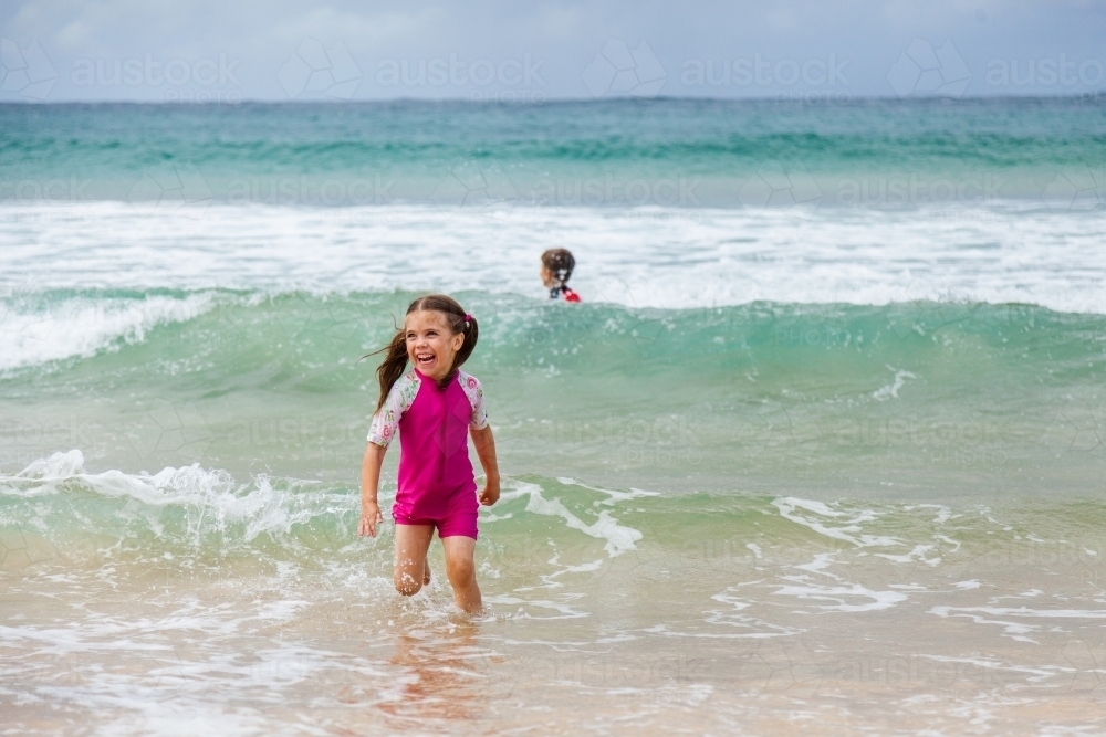 Happy kid running and splashing in seaside waves at the beach - Australian Stock Image