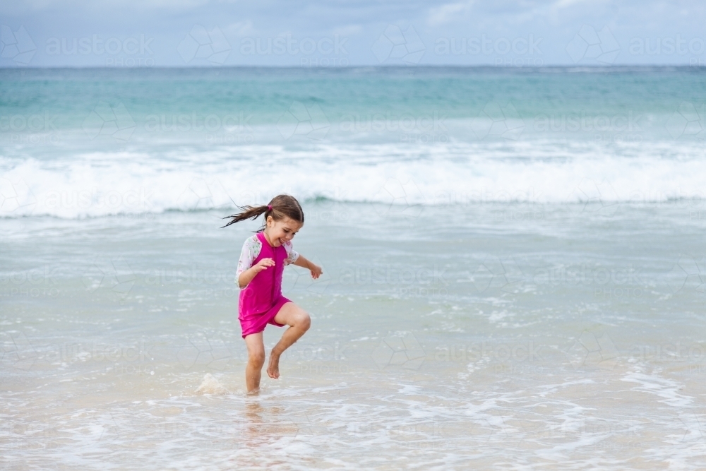 Happy kid running and splashing in seaside waves at the beach - Australian Stock Image